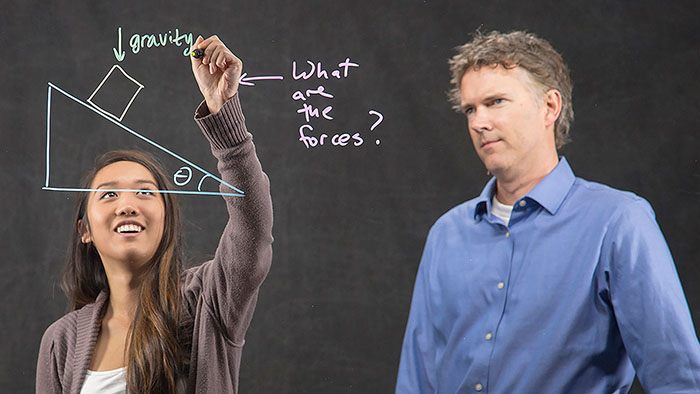 A professor watches a student diagram a physics problem on the Learning Glass